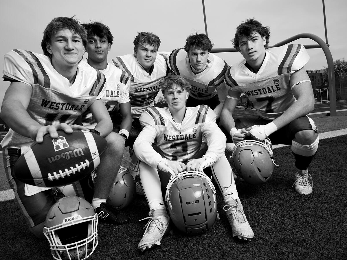 6 boys holding footballs on a football field 